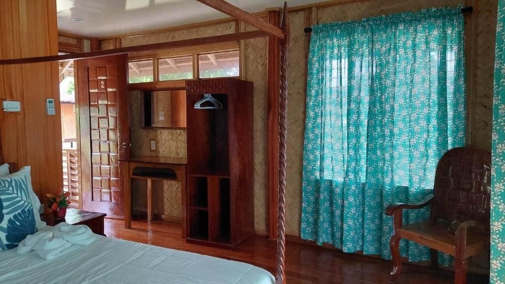 A wooden room with a bed, a wooden cabinet, a chair, and a window with floral curtains.
