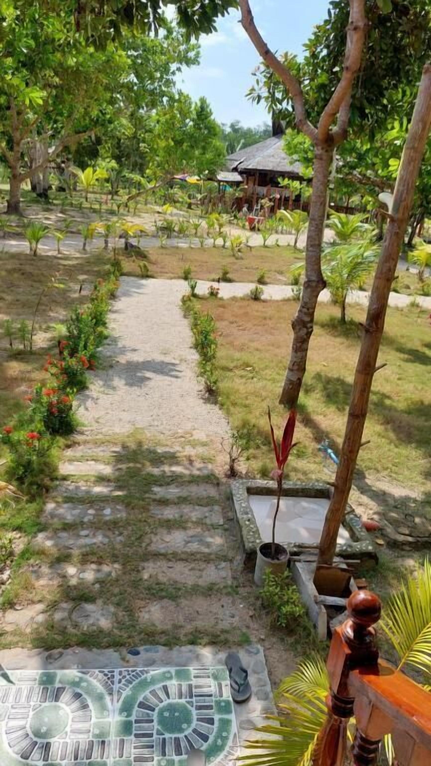 A garden pathway with a thatched-roof structure in the background.