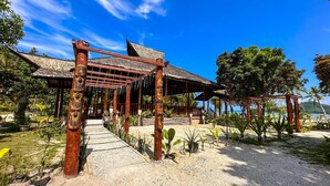 Un complexe hôtelier tropical doté d’un pavillon à toit de chaume, d’un sentier de gravier et d’une végétation luxuriante.