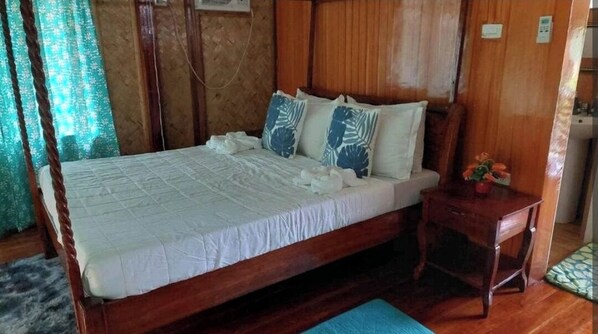 Un lit en bois avec une literie blanche et des coussins à motifs bleus, une petite table de chevet en bois avec un vase de fleurs, et un tapis bleu sur le sol.