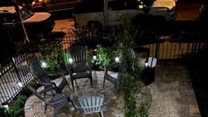 Een buitenpatio met een ronde tafel en stoelen, omringd door potplanten en een kleine boom.