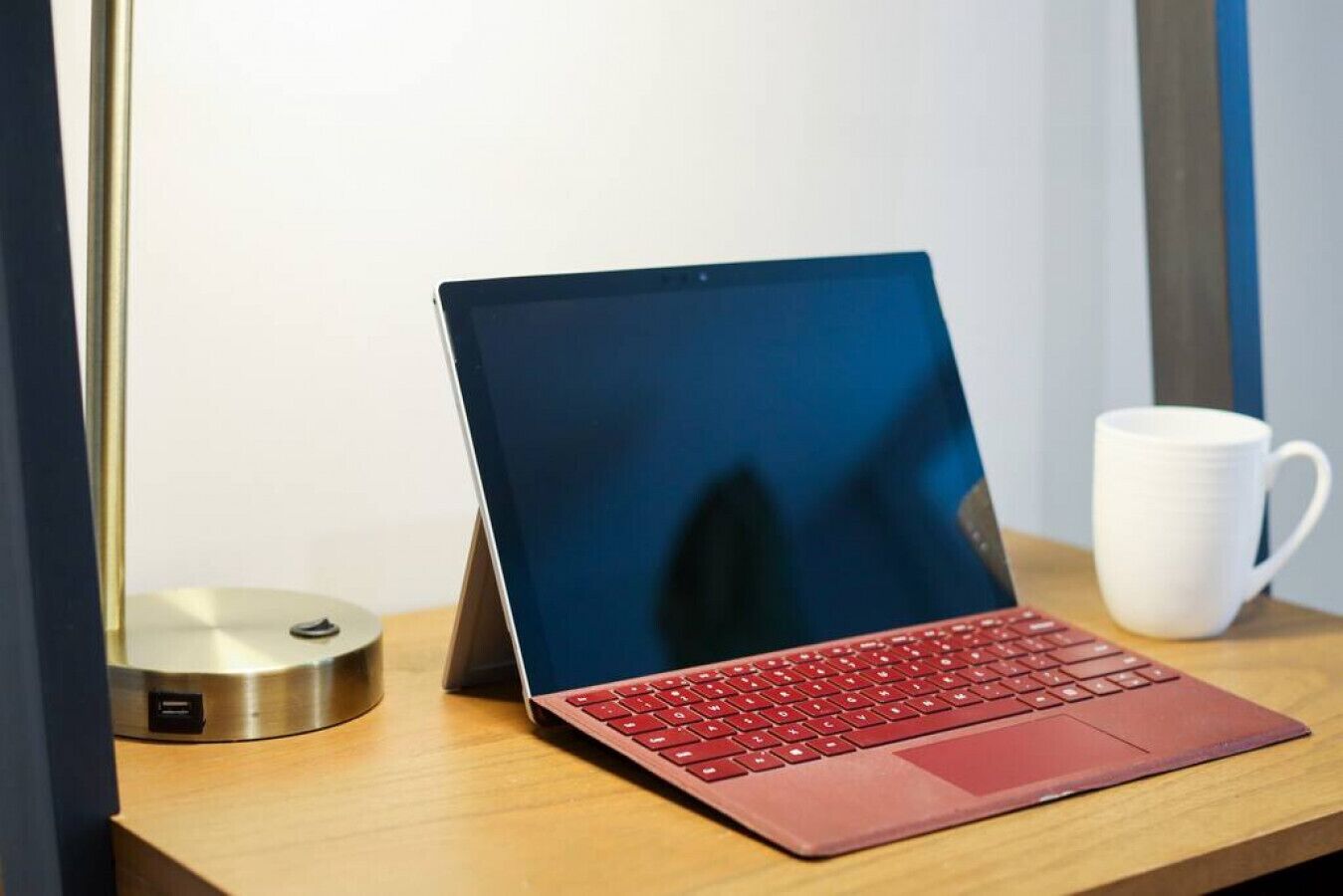 A laptop on a wooden desk with a white mug and a desk lamp.
