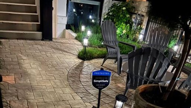 Een terras met stenen bestrating en een bordje met de tekst dat een beveiligd SimpliSafe systeem aanwezig is.