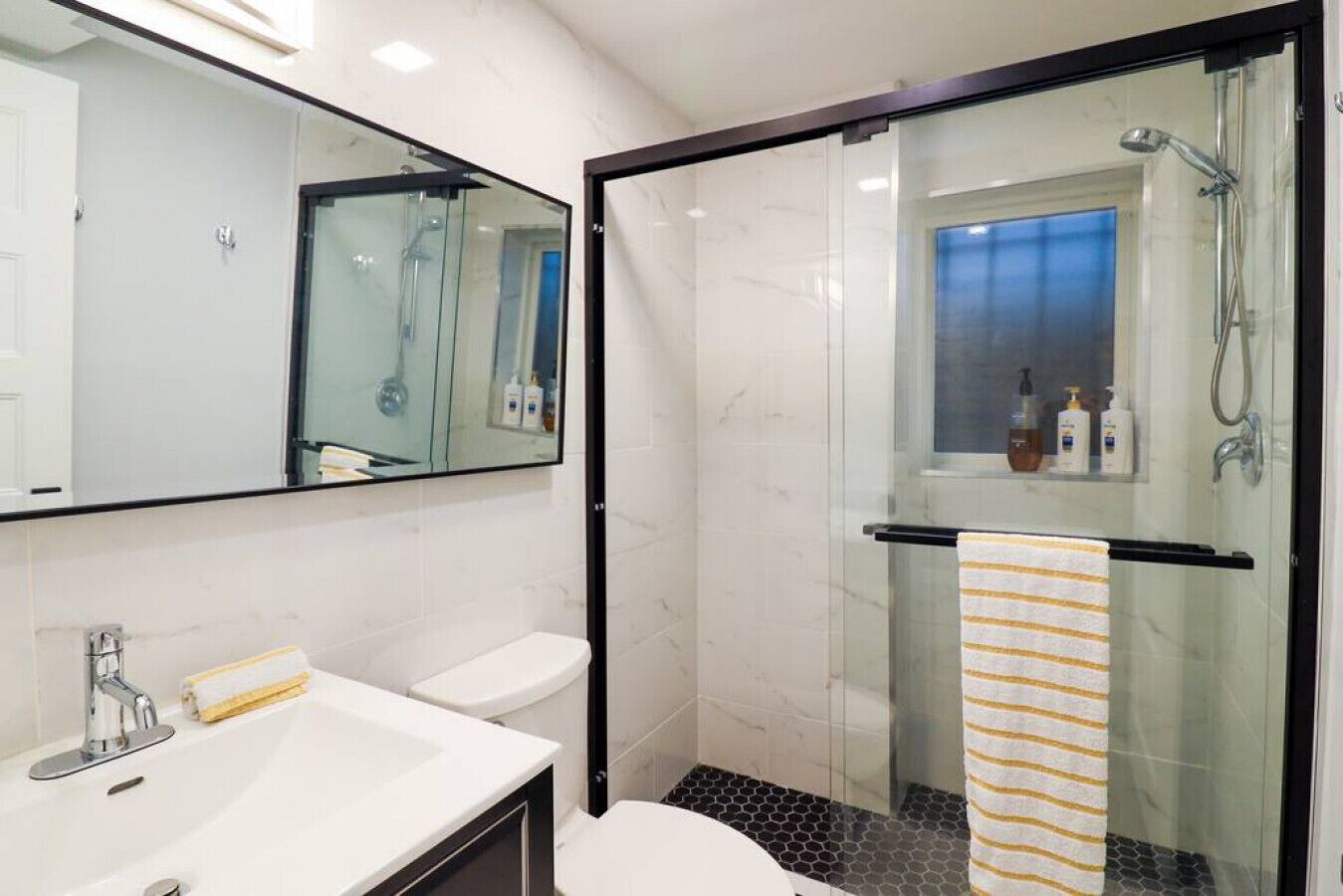 A modern bathroom with a glass-enclosed shower, a white sink, and a mirror.