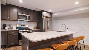 Een moderne keuken met donkere kastjes, roestvrijstalen apparatuur, een marmeren eiland en oranje barkrukken.