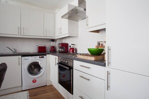 Eine moderne Küche mit weißen Schränken, einer Waschmaschine, einer Kaffeemaschine und einer grünen Schüssel auf der Arbeitsplatte.