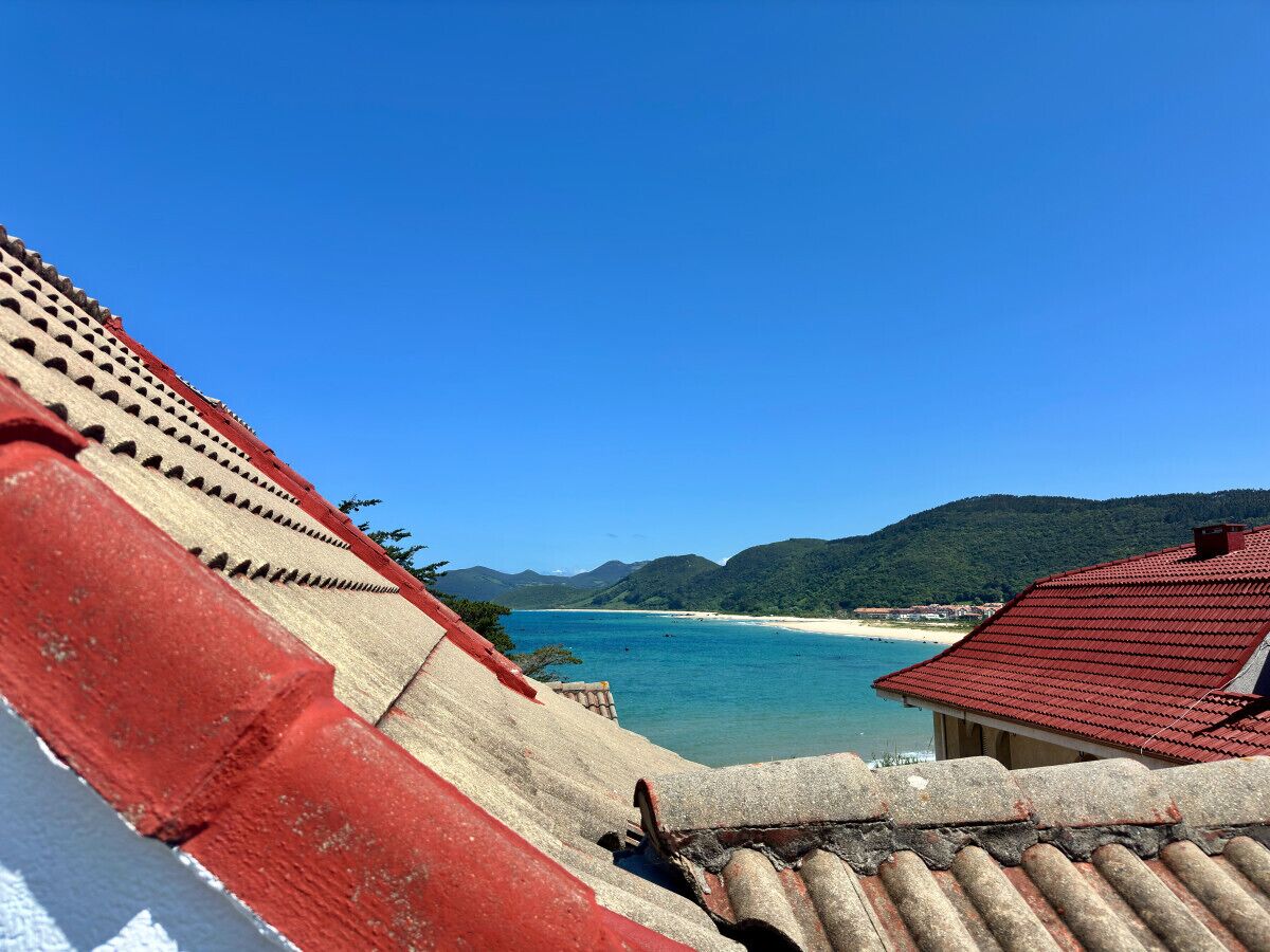 A coastal view with a clear blue sky, a sandy beach, and a mountainous backdrop.