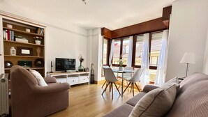 A living room with a sofa, a TV, a dining table with chairs, and a bookshelf.