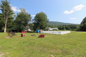 Relax in a serene grassy field with seating options and a fenced area surrounded by trees and a hill.
