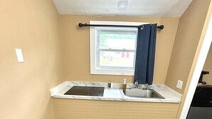 A compact kitchenette with a window, a sink, and a patterned carpet. - The Villager Motel (Bartlett)