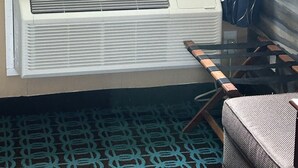 A room with a window, an air conditioning unit, a patterned carpet, and a chair. - The Villager Motel (Bartlett)