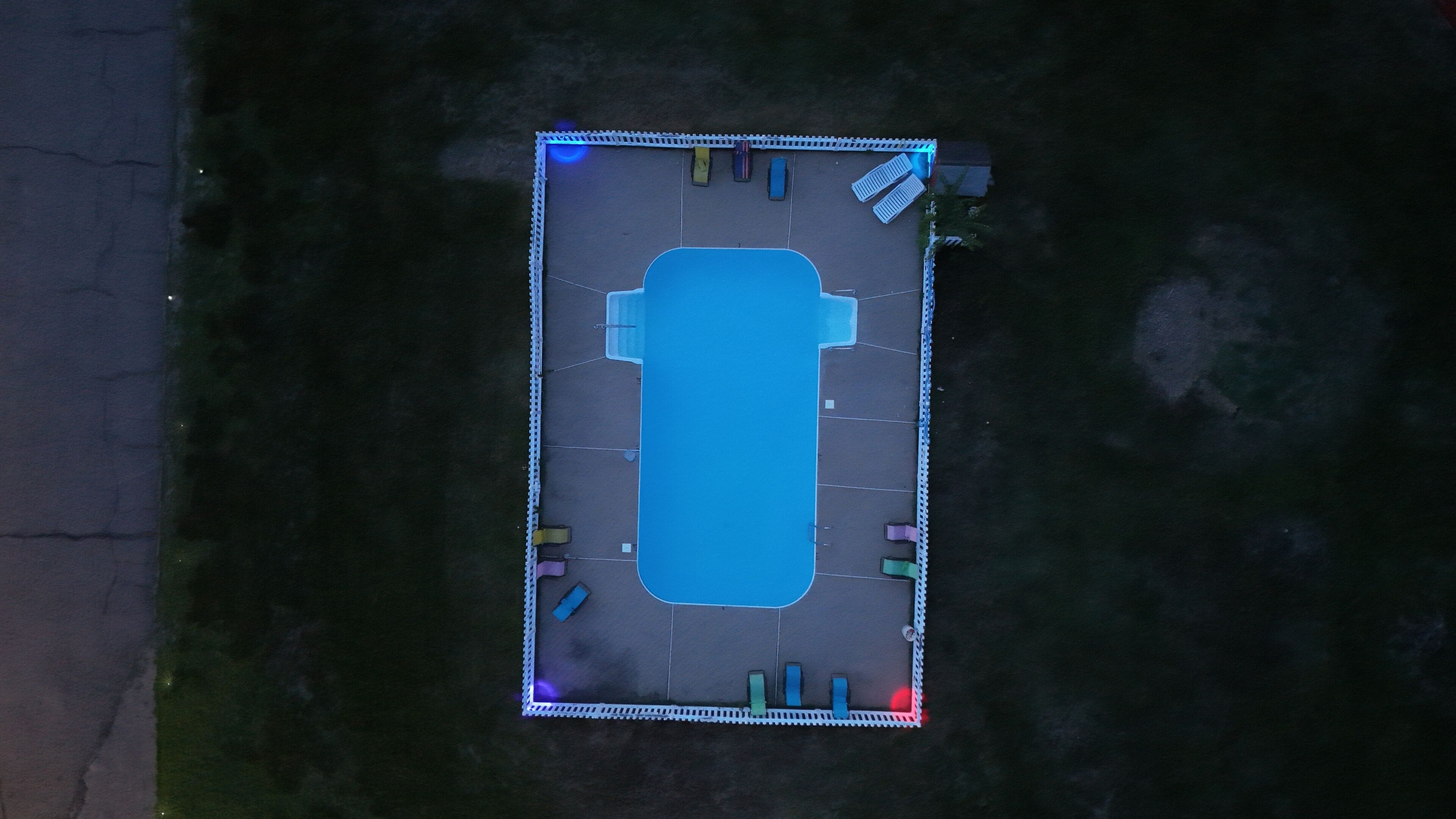Une vue aérienne d’un parking rectangulaire avec une piscine bleue au centre, entourée d’une clôture blanche.