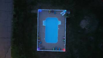 Luchtbeeld van een rechthoekige parkeerplaats met een blauw zwembad in het midden, omringd door een witte hek.