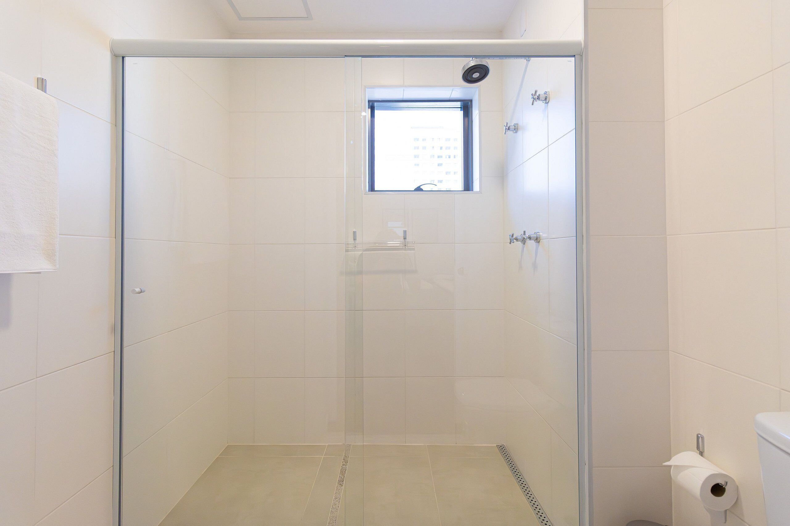 Une salle de douche moderne dotée d’une porte en verre, d’une petite fenêtre et de toilettes avec un distributeur de serviettes en papier.