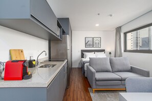 A compact living space with a kitchenette, a grey sofa, and a bed with a headboard. - Arte Arquitetura Vila Mariana (São Paulo)