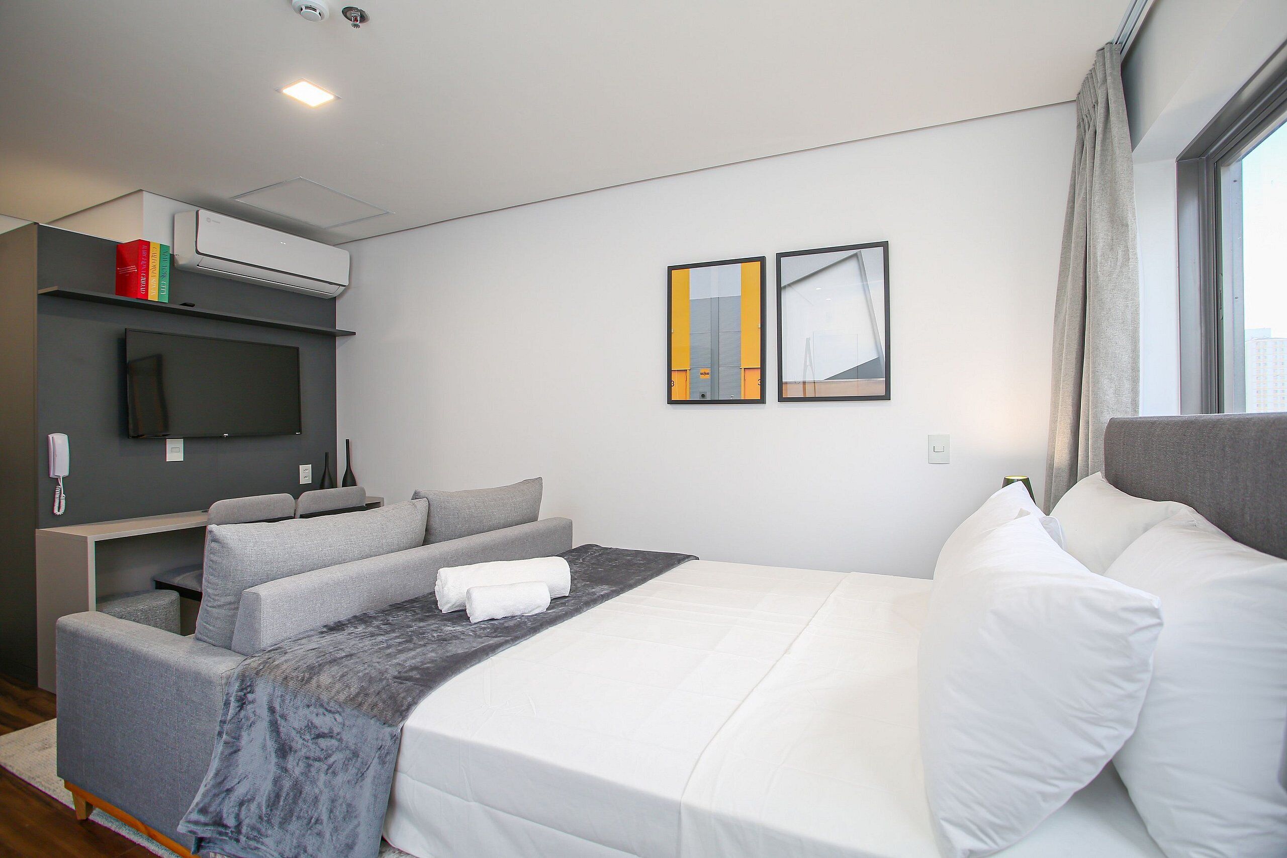 A modern hotel room with a bed, a sofa, a desk, and a flat-screen TV.