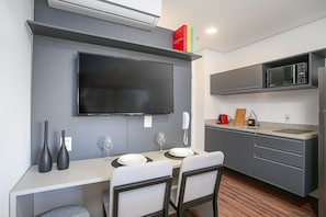 Uma cozinha moderna com televisão de tela plana, micro-ondas e área de jantar com mesa posta para dois.