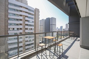 A balcony with four wooden tables and chairs, overlooking a cityscape with high-rise buildings. - Arte Arquitetura Vila Mariana (São Paulo)