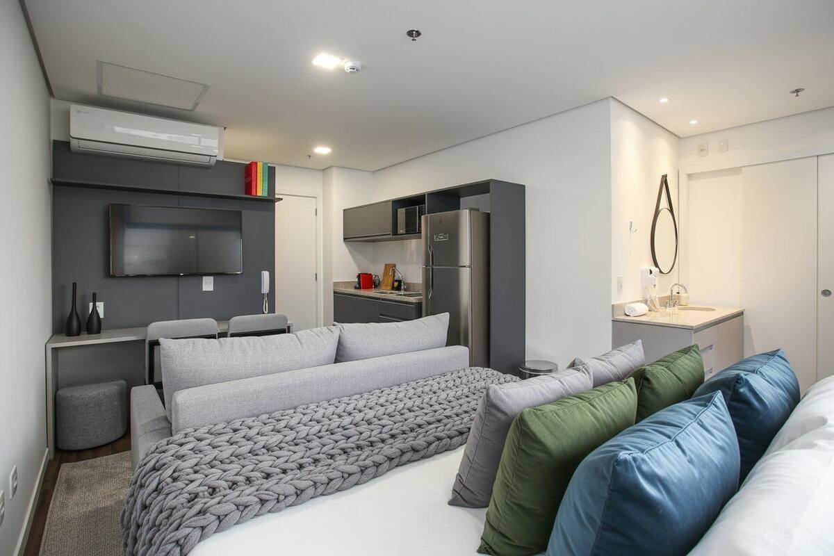 A compact bedroom with a bed, a TV, a kitchenette, and a bathroom.