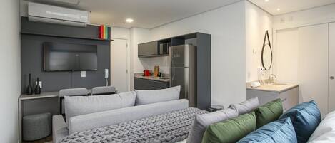 A compact bedroom with a bed, a TV, a kitchenette, and a bathroom.