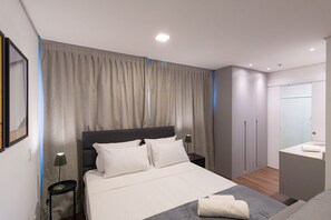 Ein modernes Schlafzimmer mit einem großen Bett, einem Nachttisch, einem Schrank und einem Badezimmer mit Spiegel und Waschbecken.
