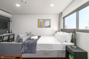 Quarto de hotel moderno com cama, escrivaninha e uma janela grande.