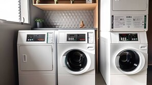 Un espace buanderie compact comprenant deux machines à laver à chargement frontal et une petite étagère ornée d’objets décoratifs.