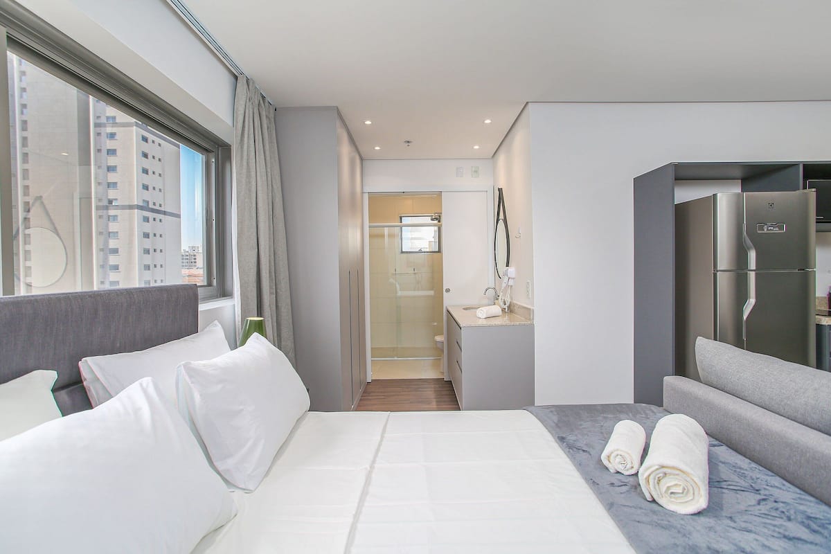 A modern hotel room with a bed, a seating area, a bathroom, and a view of the city.