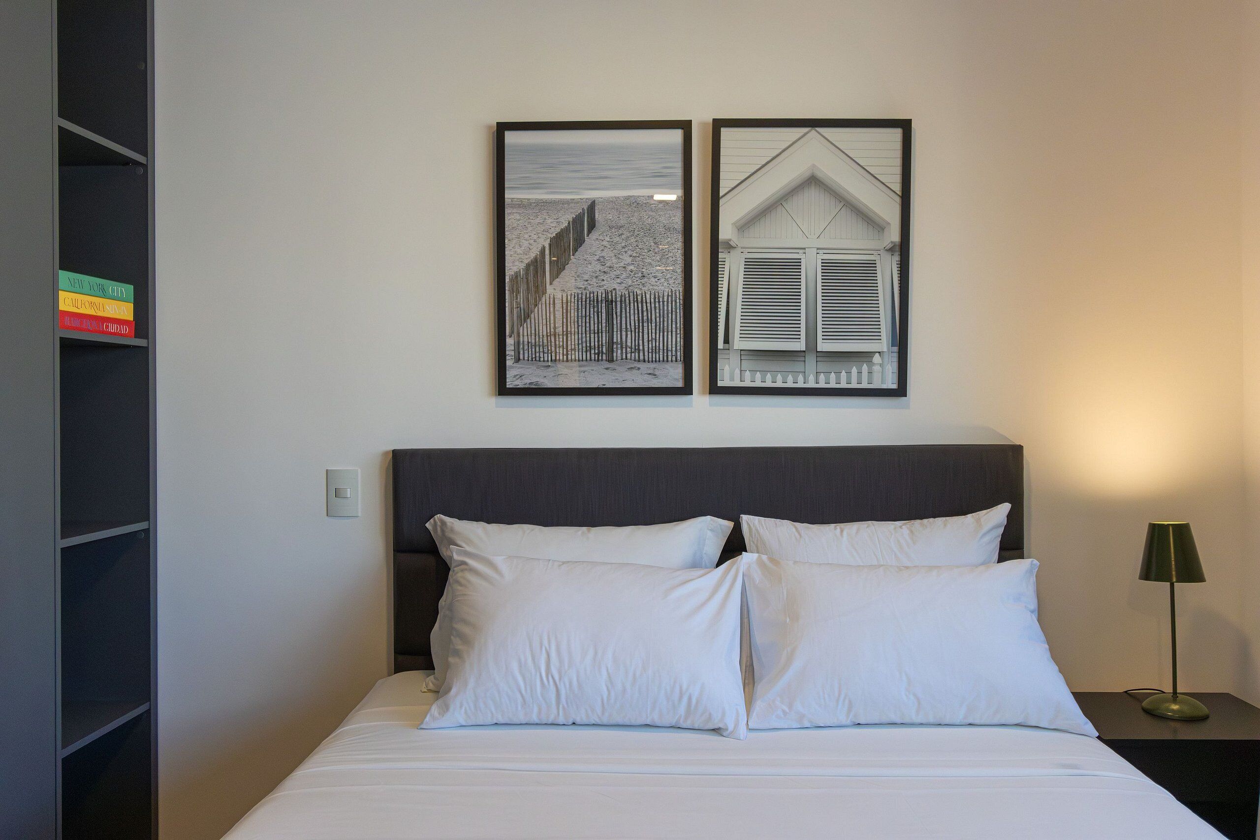 A neatly made bed with white linens, a dark headboard, and a bedside lamp.