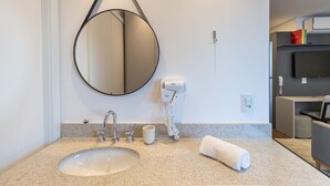 Une salle de bain moderne avec un miroir rond, un lavabo, un sèche-cheveux, une tasse et une serviette posés sur le comptoir.