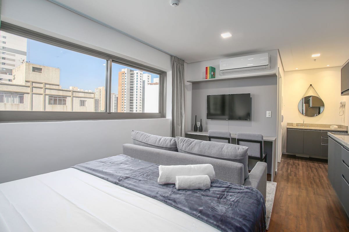 A modern hotel room with a large bed, a desk, a flat-screen TV, and a view of the cityscape.