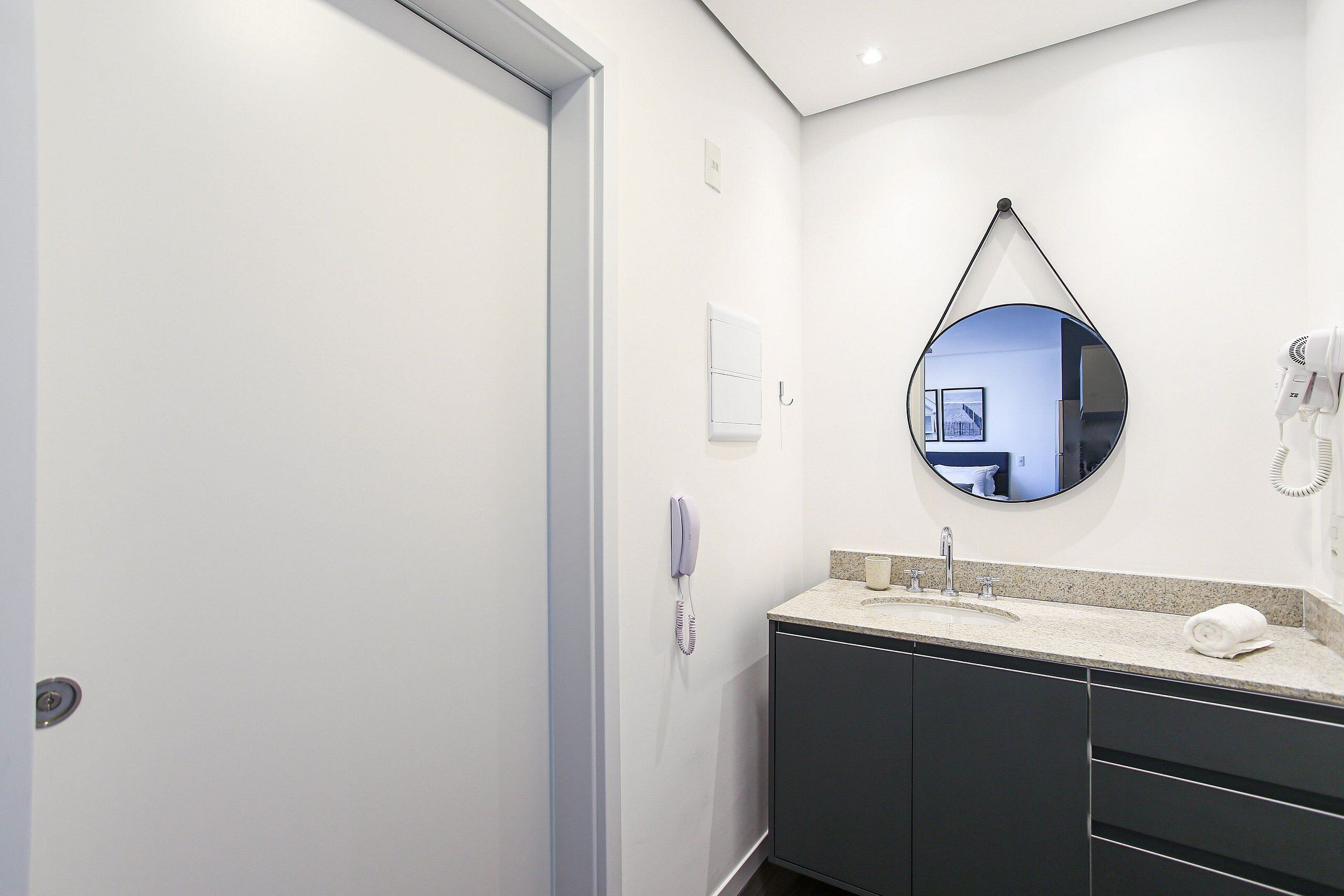 Een moderne badkamer met een witte deur, een ronde spiegel, een wastafel en een haardroger.