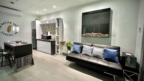 A modern living room with a leather sofa, a dining area with a kitchen in the background, and a large window with a decorative view. - Luxury Tiny home with pool & amazing view (Caguas)