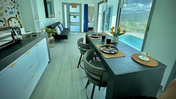 A modern kitchen with a dining area, a sofa, and a view of a swimming pool. - Luxury Tiny home with pool & amazing view (Caguas)