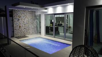 A modern outdoor pool area with a water feature and a glass-enclosed patio.