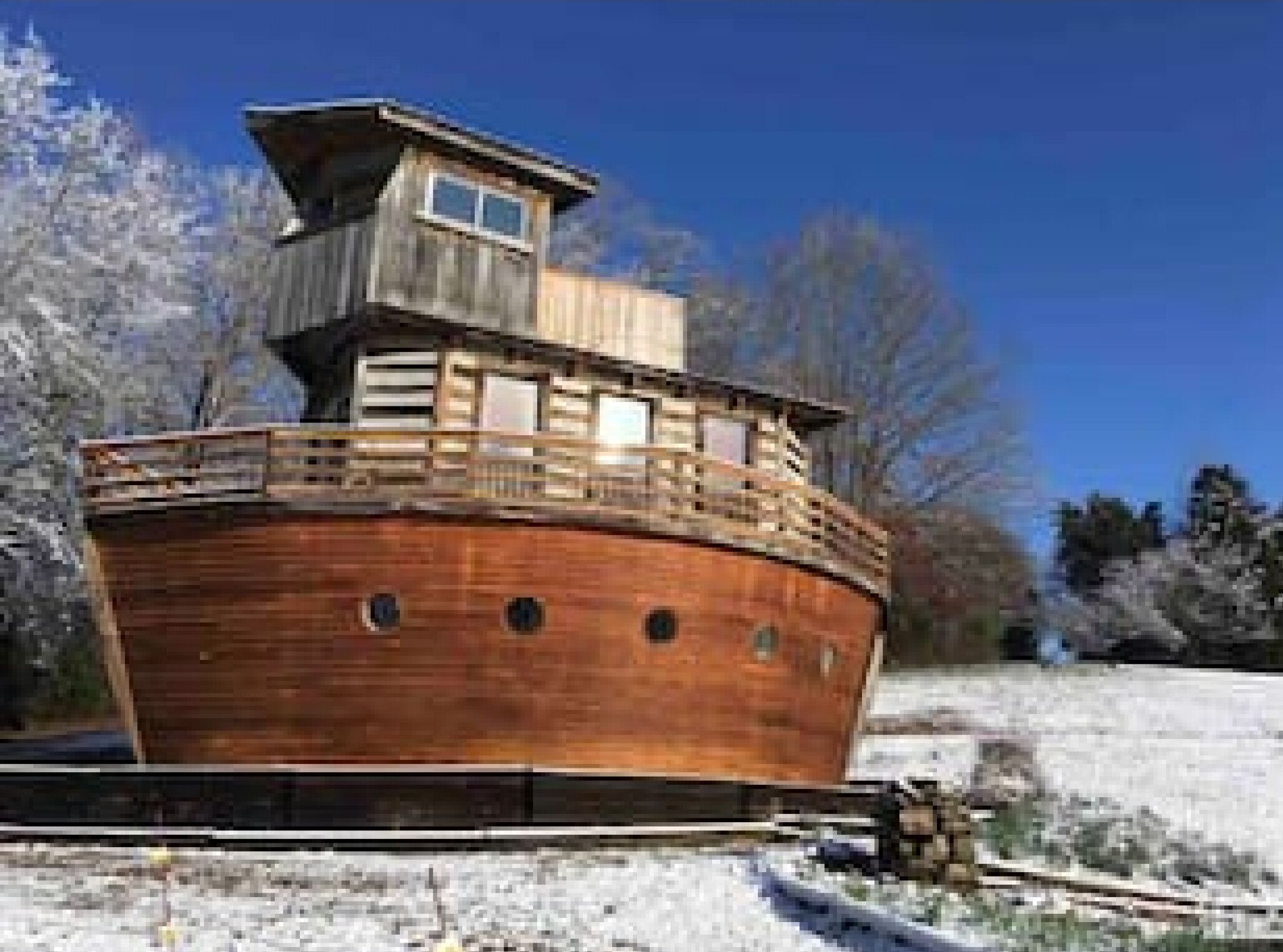 A large wooden boat with a cabin structure on top, surrounded by snow and trees.