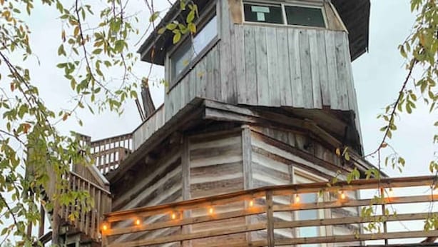 Una cabaña de madera con balcón, escaleras y puerta que da al interior.