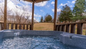 Ein Whirlpool mit einer Holterrasse und Blick auf ein Wiesenfeld und Bäume.
