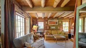 Ein Holzblockhaus-Innenraum mit Holzbalkendecke, großen Fenstern, einer Couch, einem Couchtisch und einer Lampe.