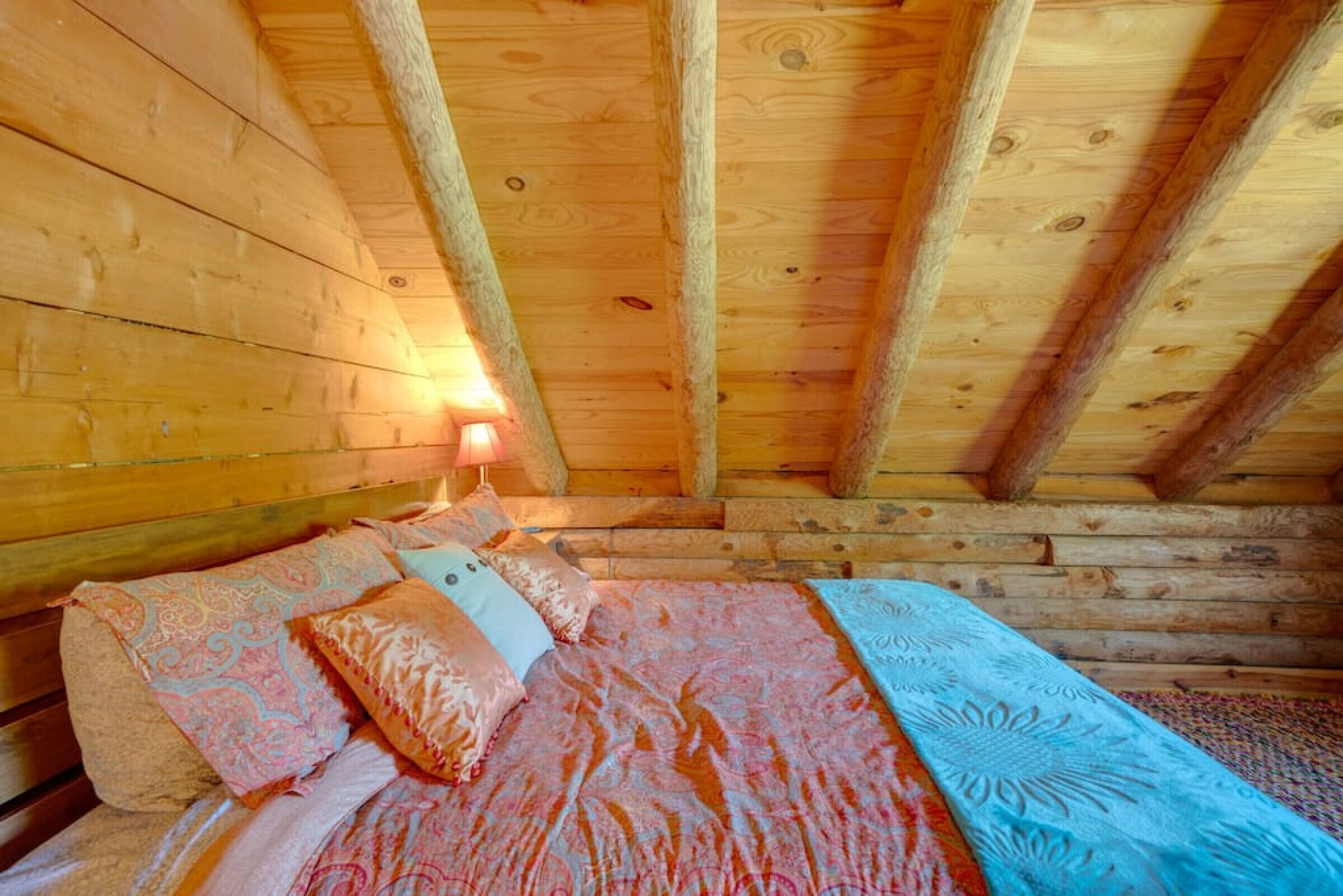 Una habitación de cabaña de madera con una cama, almohadas y una mesita de noche con lámpara.