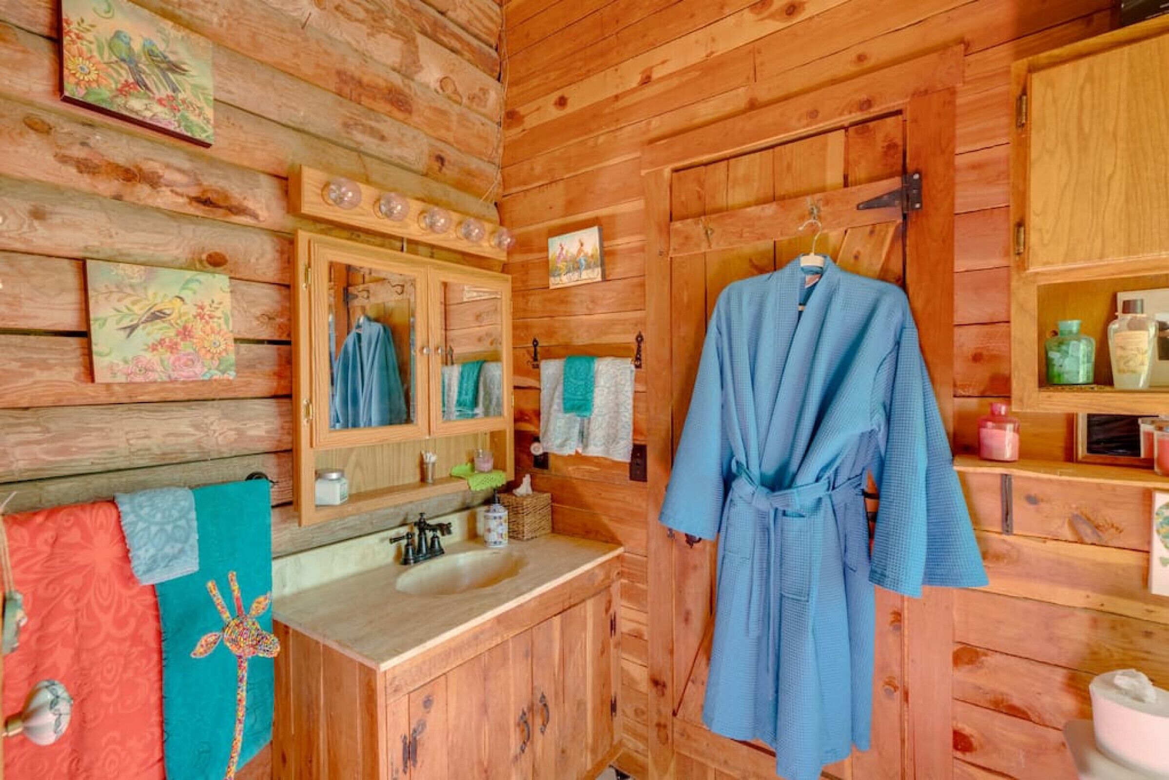 Une salle de bain rustique, avec une cabine en bois, un lavabo en bois, un miroir et une robe accrochée au mur.