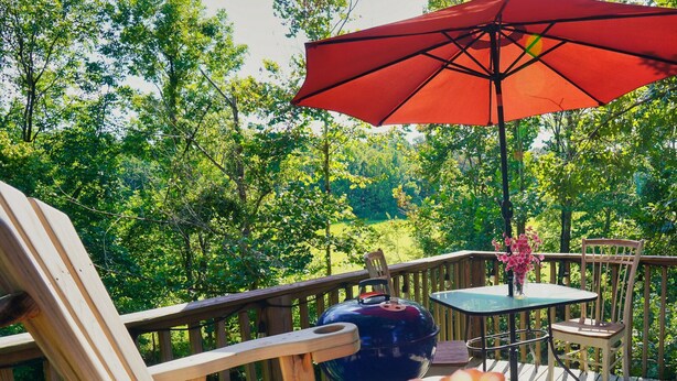 Une terrasse en bois avec un parasol rouge, une table et des chaises.