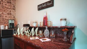 Un comptoir de cuisine surmonté d’un plateau en marbre, une machine à café, une bouteille de boisson rouge et de la verrerie décorative.