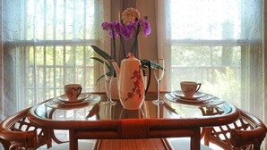 Une table à manger ornée d’un vase contenant des orchidées violettes, de deux tasses et d’une théière.