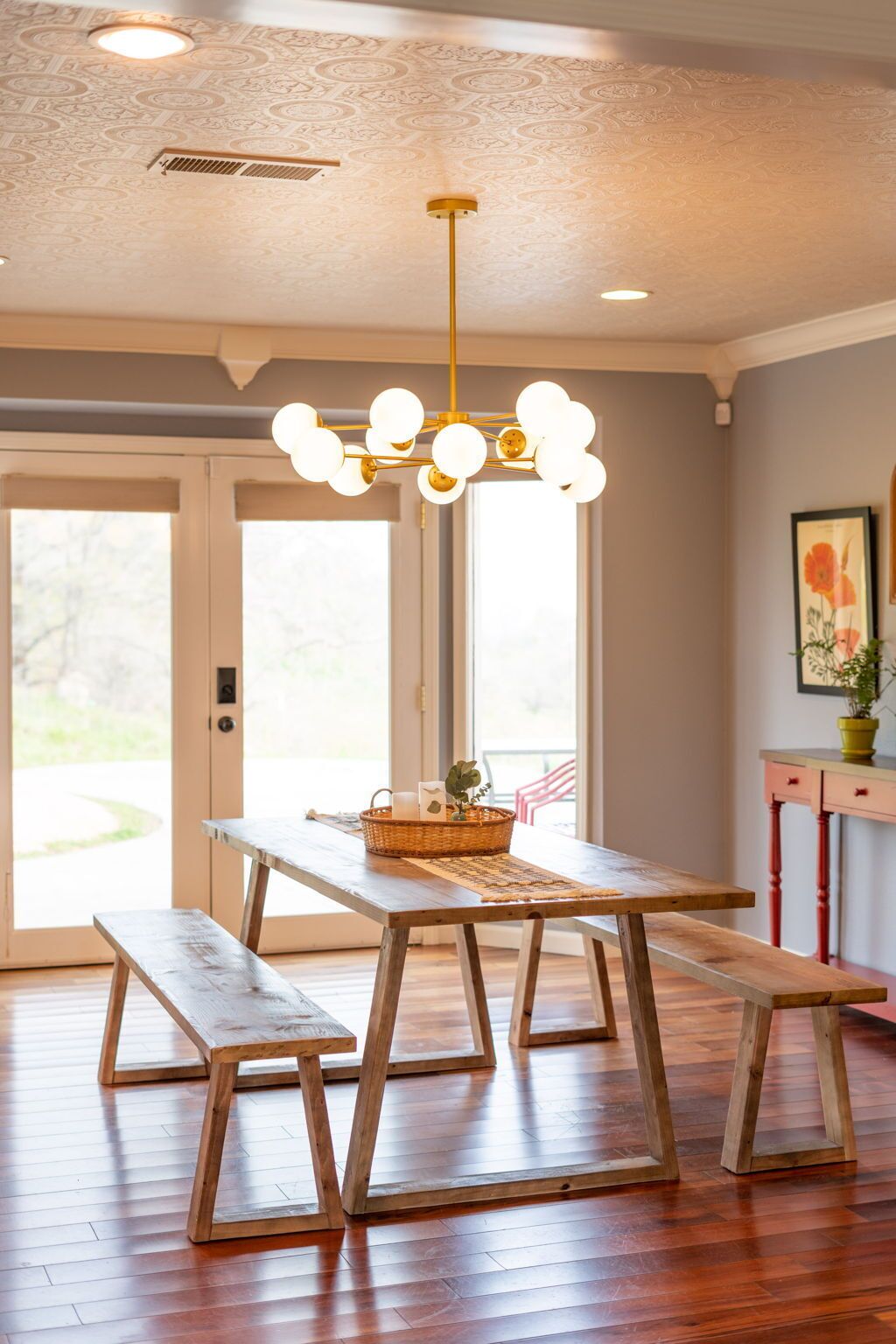 A dining area with a wooden table and benches, a hanging light fixture, and a door leading outside.