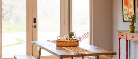 A dining area with a wooden table and benches, a hanging light fixture, and a door leading outside.