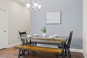 Un coin repas avec une table en bois, des chaises noires, un banc, un vase avec une plante et un lustre.