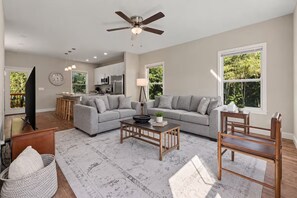 A spacious living room with a grey sofa, a wooden coffee table, and a ceiling fan.