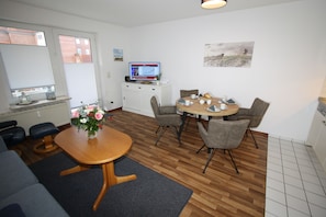 A modern living room with a wooden dining table, grey sofas, and a TV on a cabinet.