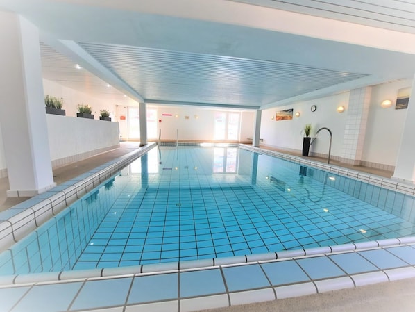 An indoor swimming pool with clear blue tiles, a tiled floor, and a ceiling with a grid pattern.